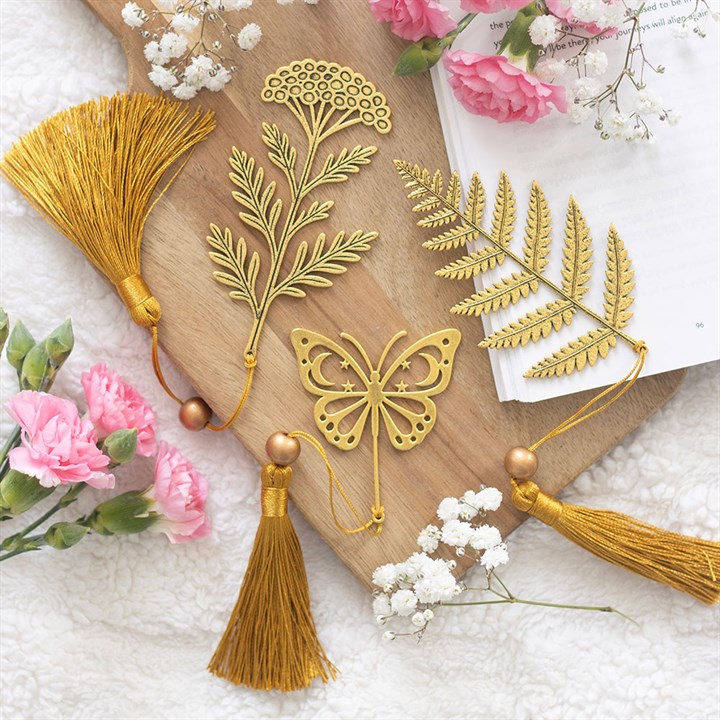 Gold decorative items with tassels and floral designs on a wooden board with flowers around.