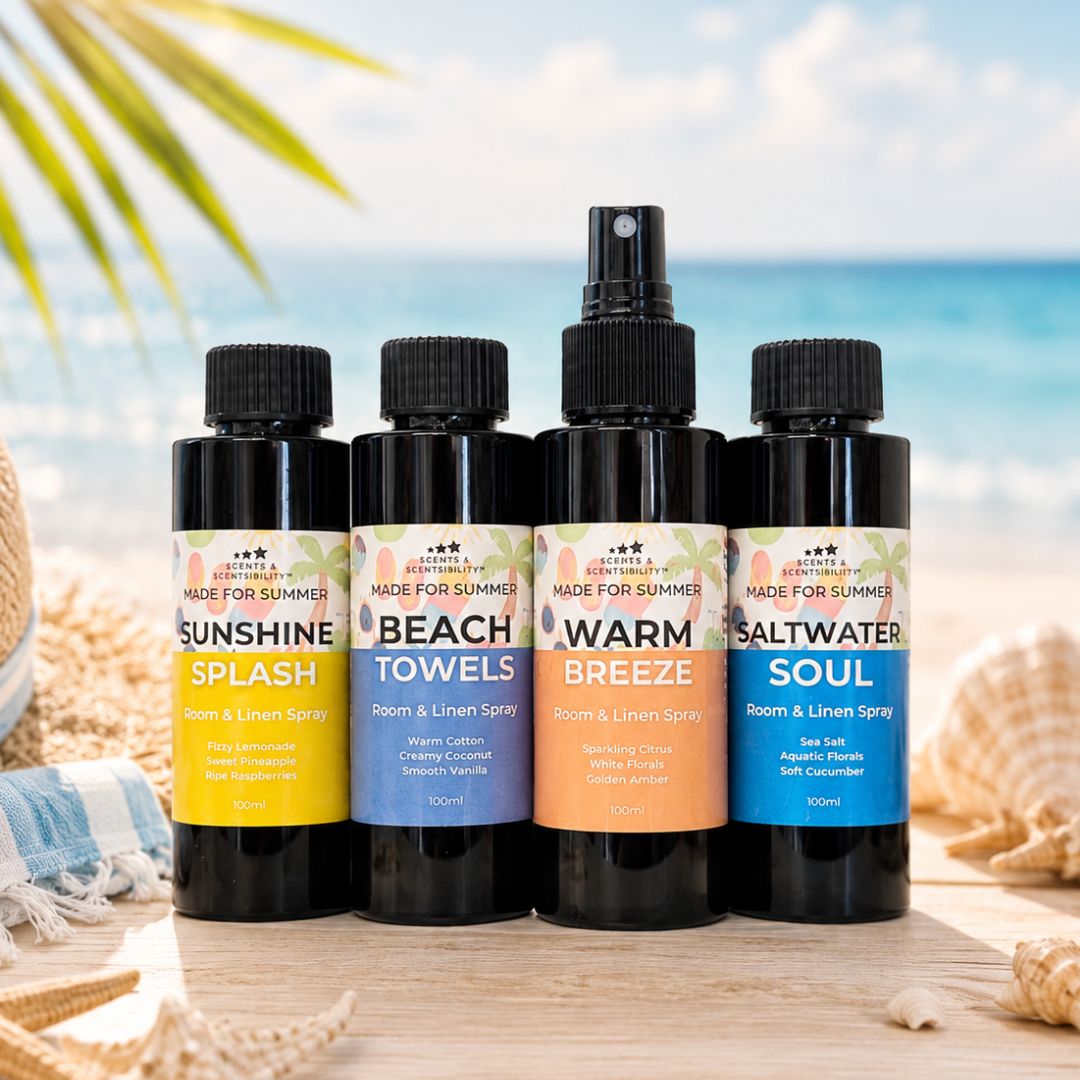 Four black room and linen spray bottles with colorful labels are arranged on a wooden surface with a beach backdrop. The labels read Sunshine Splash, Beach Towels, Warm Breeze, and Saltwater Soul, with 'Made for Summer' printed at the top of each bottle.