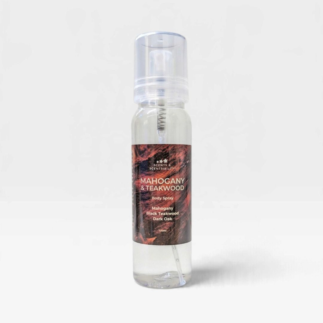 A clear plastic spray bottle of Scents & Scentsibility Mahogany & Teakwood Body Spray, filled with a transparent liquid and featuring a dark brown and red textured label, set against a plain light gray background.