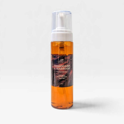A clear plastic pump bottle filled with amber-orange liquid, featuring a white pump and a dark brown label that reads 'Mahogany & Teakwood'. The bottle is centered against a clean, light gray background with a soft shadow.