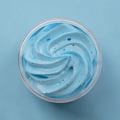 A top-down view of light blue whipped soap swirled inside a clear plastic round container, set against a solid light blue background.