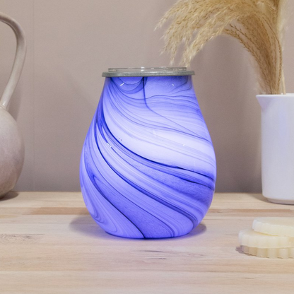 Blue and white marbled glass wax melt warmer on a wooden surface with decorative items in the background.