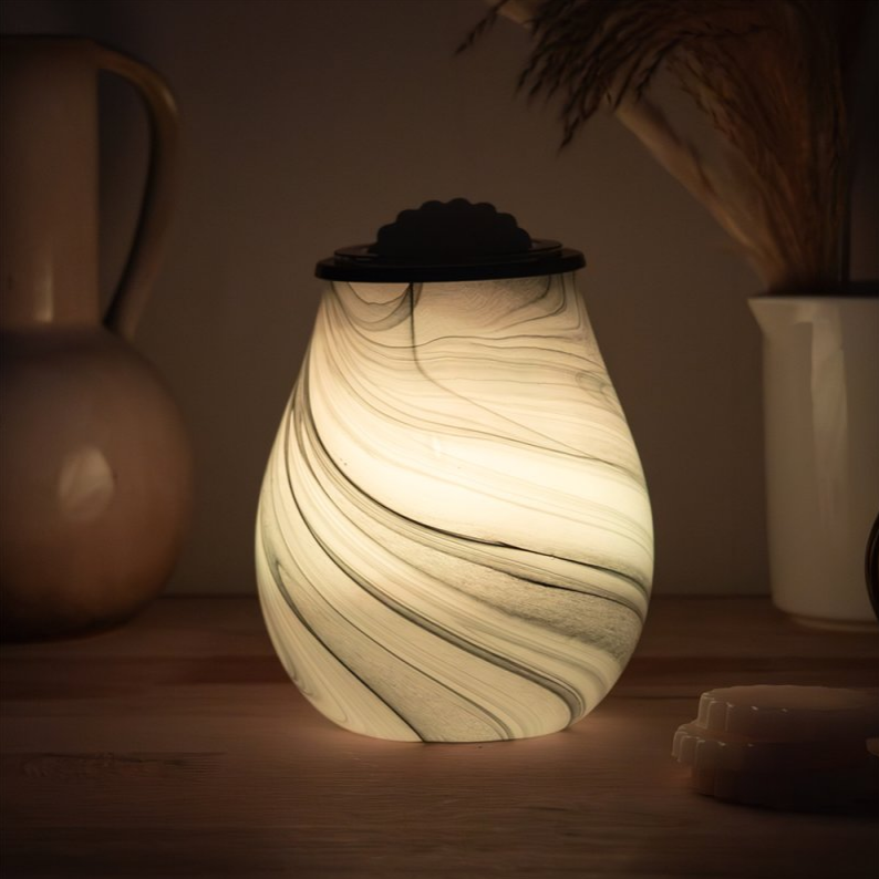 Marble-patterned wax melt warmer on a wooden surface with a warm glow