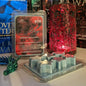Scented wax melt packaging with a red candle and decorative items on a surface.