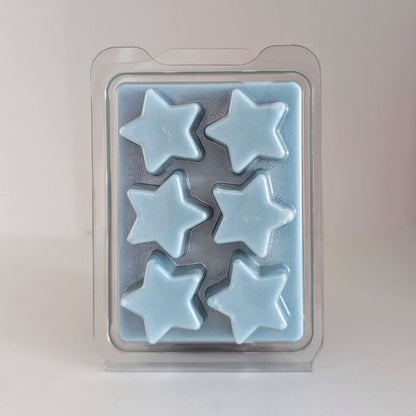 Pale blue star-shaped wax melts in a clear plastic packaging on a light gray background
