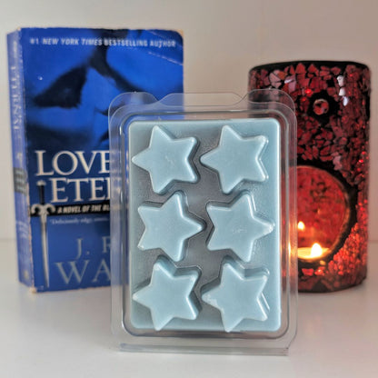 Star-shaped wax melts in a clear plastic packaging with a book and decorative item in the background.