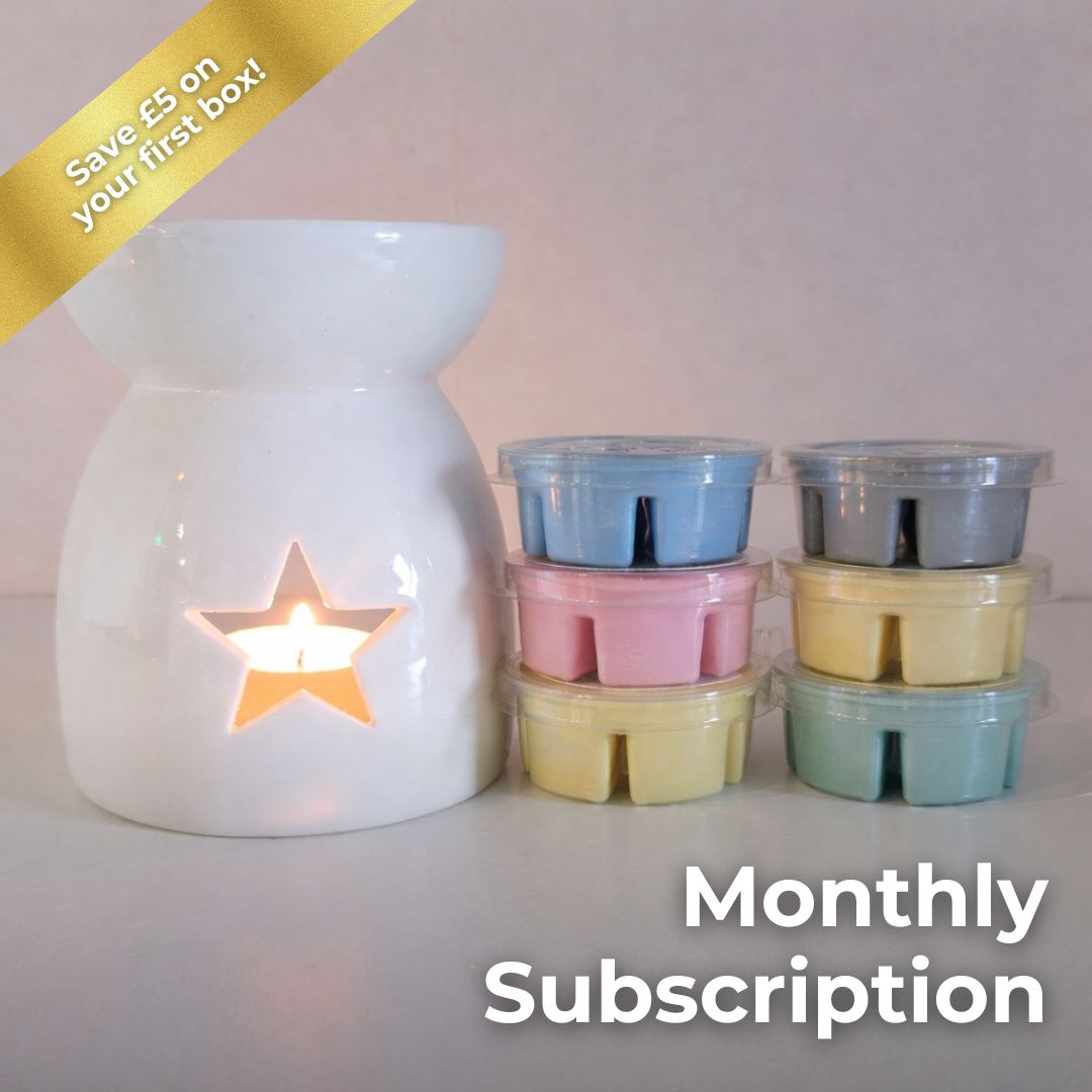 White ceramic wax melt burner with a lit candle and pastel-colored wax melts on a white background