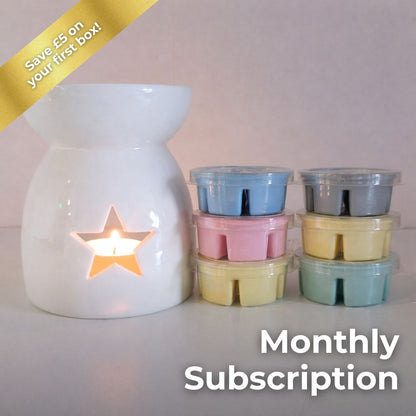 White ceramic wax melt burner with a lit candle and pastel-colored wax melts on a white background