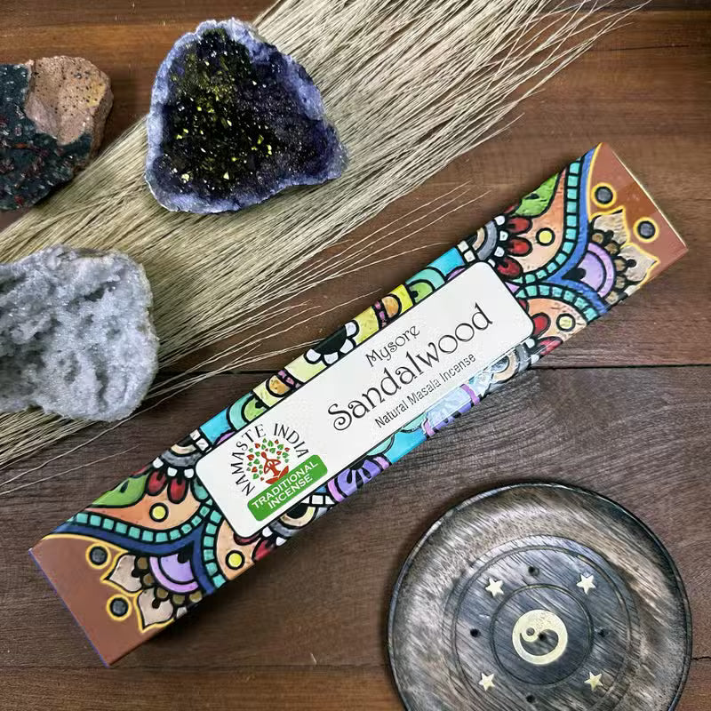Sandalwood incense stick box with decorative design on a wooden surface with crystals and a wooden plate.