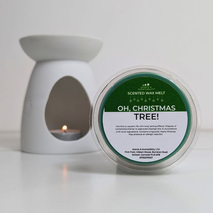 Scented wax melt container labeled 'Oh, Christmas Tree!' next to a white wax warmer with a lit candle.