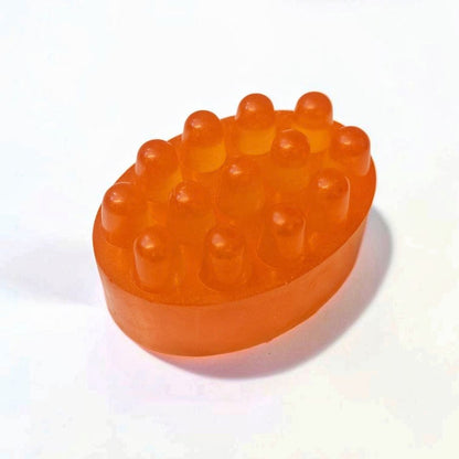 Orange oval massage soap bar with raised textured bumps on a white background.