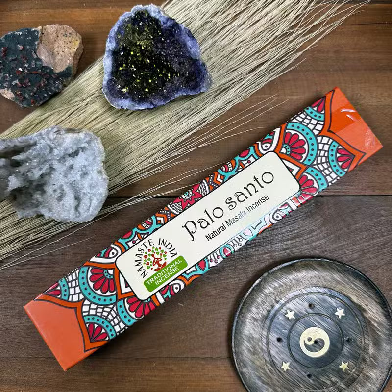 Palo Santo incense packaging with decorative elements on a wooden surface with crystals and a metal dish.