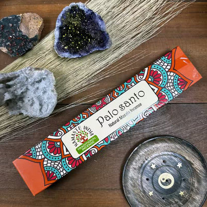 Palo Santo incense packaging with decorative elements on a wooden surface with crystals and a metal dish.