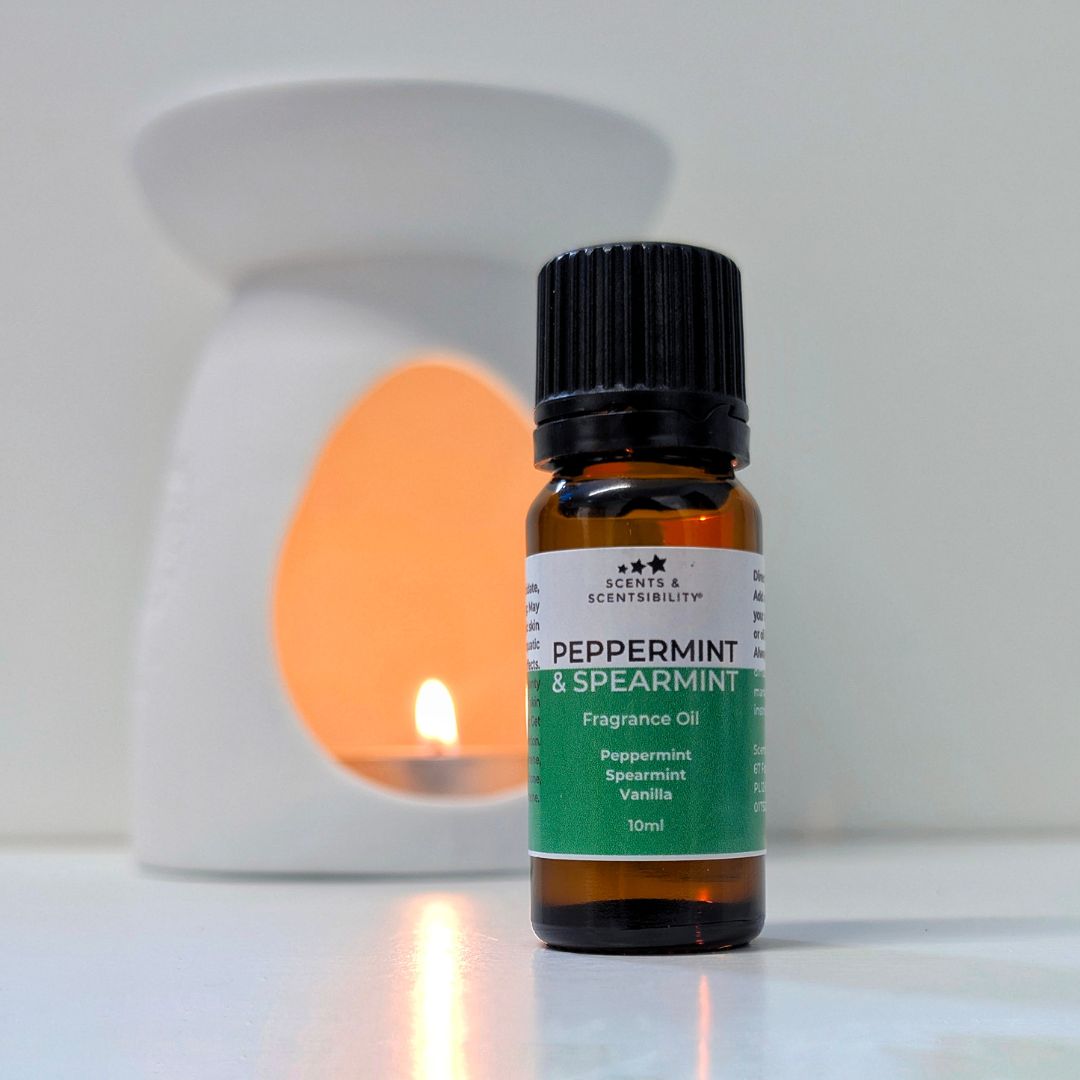 A 10ml bottle of Scents & Scentsibility Peppermint & Spearmint Fragrance Oil in an amber glass bottle with a black cap, set against a blurred white diffuser with a warm orange glow.