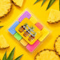 Set of colorful wax melts in a clear container with 'Poppin Pineapple' branding on a yellow background with pineapple slices.