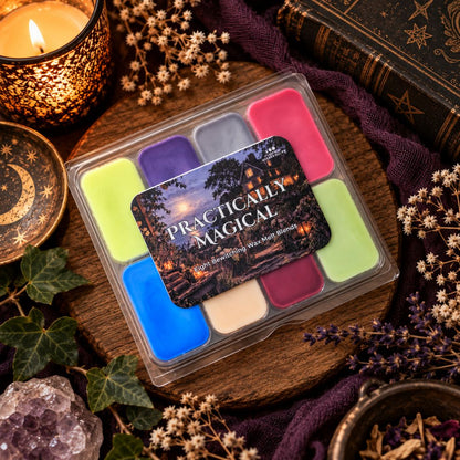 A clear plastic wax melt clamshell labeled 'Practically Magical' sits on a wooden board surrounded by dried flowers, a lit candle, books, and purple fabric. The product contains multiple pastel and bright wax blocks in green, blue, pink, purple, gray, and cream.