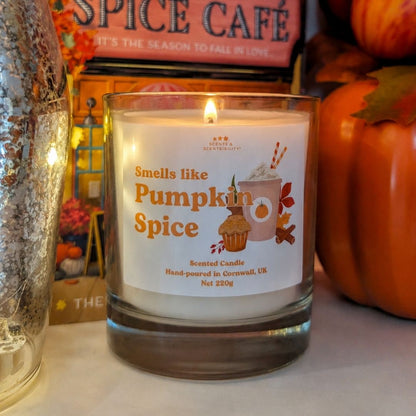 A lit candle in a glass jar labelled Smells Like Pumpkin Spice, surrounded by autumnal decor and books. 