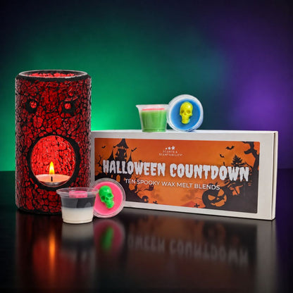 Halloween Countdown wax melt bundle by Scents & Scentsibility, featuring a red crackle wax melt burner with a lit candle, small wax melts in plastic pots, and the product box on a reflective black surface against a green and purple gradient background.