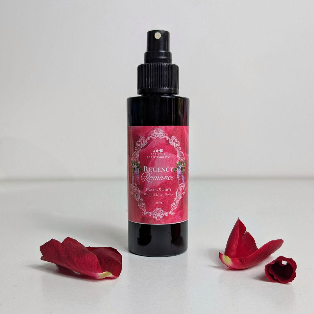 Black spray bottle with a pink label on a white background with red flower petals.