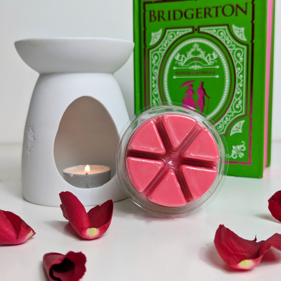 Pink wax melts in a container with a white wax warmer and red rose petals on a white background, featuring a 'Bridgerton' book.