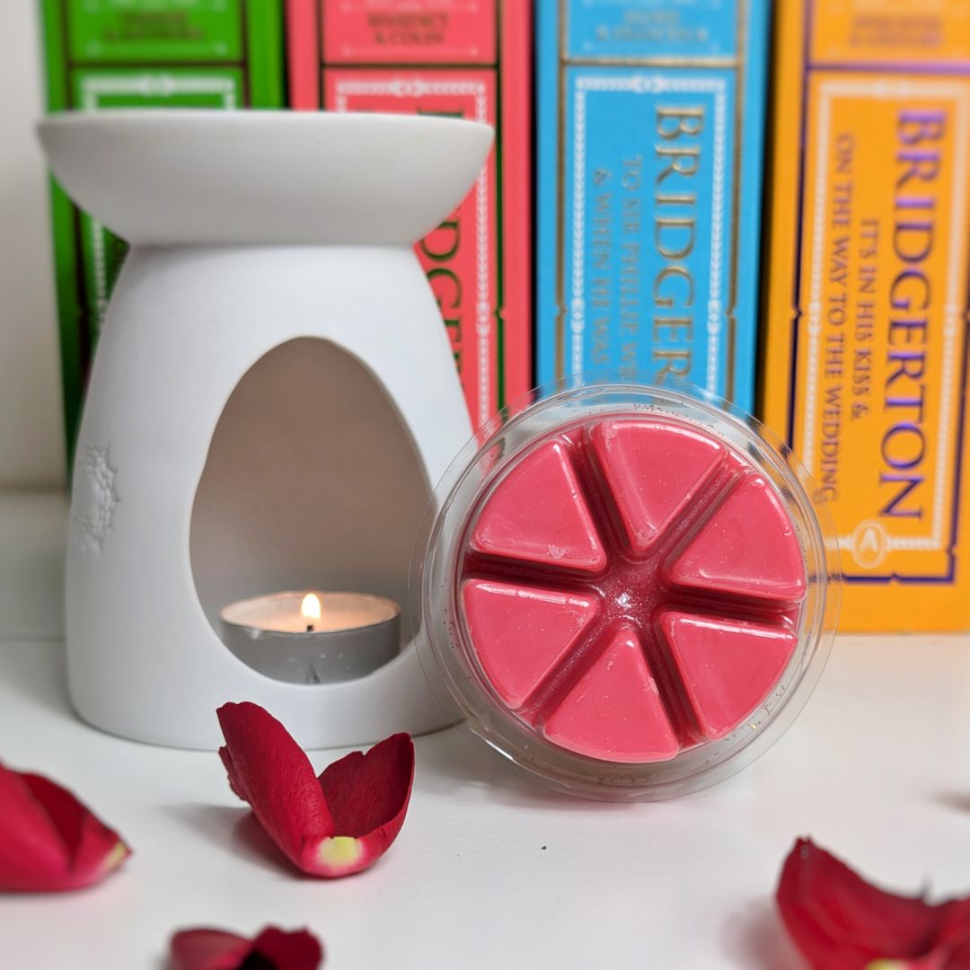 White wax warmer with a lit candle and pink wax melts in front of 'Bridgerton' books.