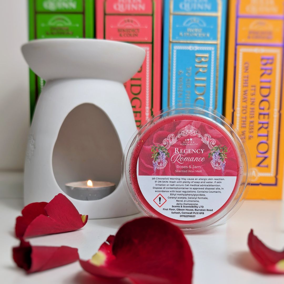 White wax warmer with a lit candle and 'Regency Romance' wax melt container in front of 'Bridgerton' themed books.
