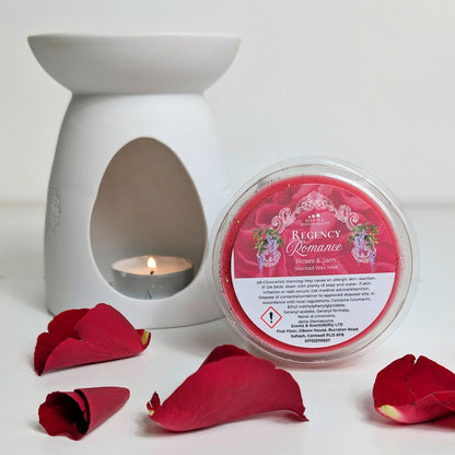 White wax warmer with a lit candle and red rose petals on a white background