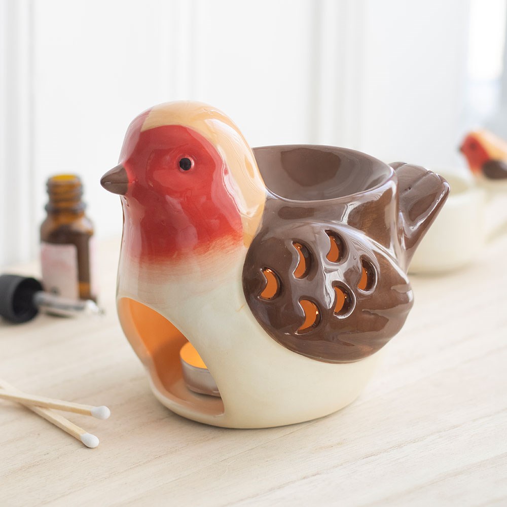 Robin Shaped Ceramic Wax Melt and Oil Burner on a wooden surface with a lit tealight glowing through its decorative wing cut-outs, creating a cosy atmosphere.