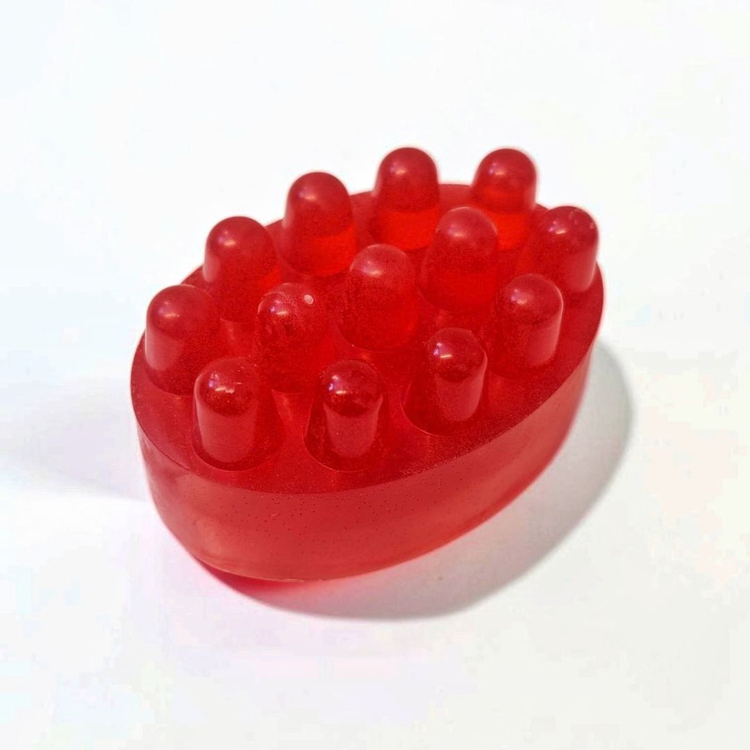 Red oval massage soap bar with raised textured bumps on a white background.