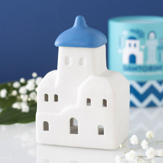 White ceramic oil burner and wax warmer with blue roof on a white surface with flowers and a blue background