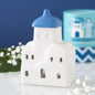 White ceramic oil burner and wax warmer with blue roof on a white surface with flowers and a blue background
