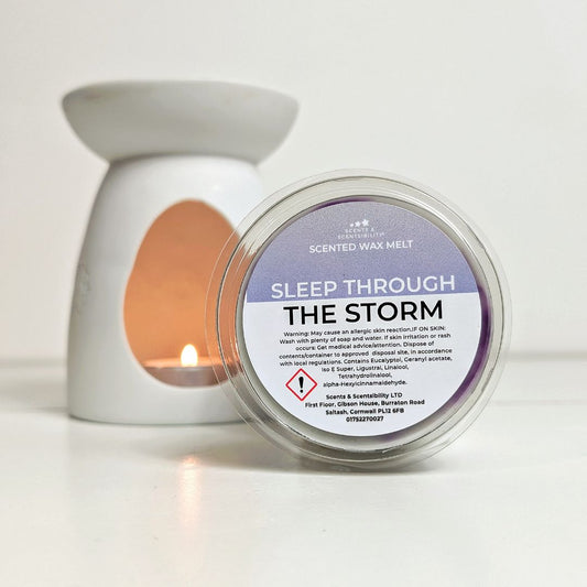 Scented wax melt container labeled 'Sleep Through The Storm' with a lit candle in the background.