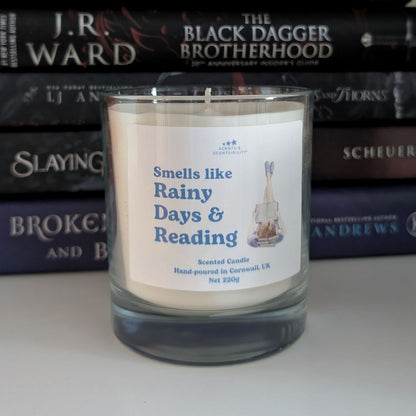 Candle with a label 'Smells like Rainy Days & Reading' in front of stacked books