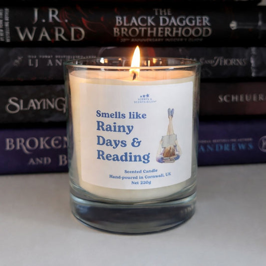 Candle labeled 'Smells like Rainy Days & Reading' in front of stacked books