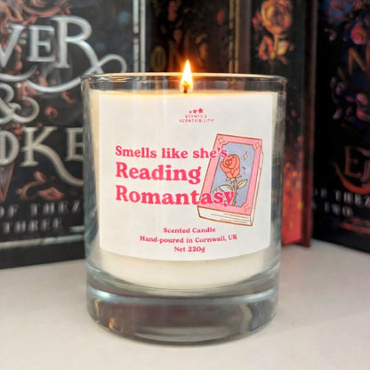 Candle with a label reading 'Smells like she's reading Romantasy' in front of books.