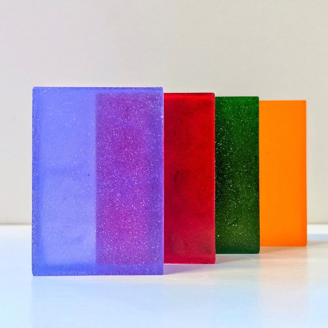 Colourful rectangular soap bars in purple, red, green and orange, displayed together on a white background.