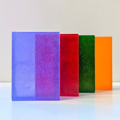 Colourful rectangular soap bars in purple, red, green and orange, displayed together on a white background.