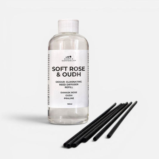Clear bottle of 'Soft Rose & Oudh' reed diffuser with black sticks on a white background