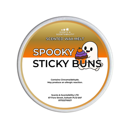 A round tub of Scents & Scentsibility 'Spooky Sticky Buns' scented wax melt, featuring a white and orange label with a cartoon ghost and cake illustration.