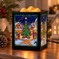 A square black wax melt waremer with a colorful stained-glass-style Christmas village scene on the front and side panels, shown lit with warm yellow glow on a wooden table with holiday decor in the background.