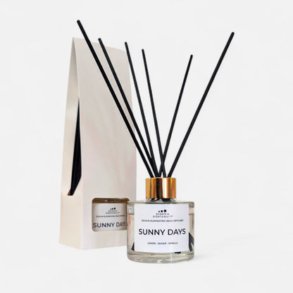 A glass bottle diffuser with clear liquid, gold collar and black fibre reeds with a white label and presentation box