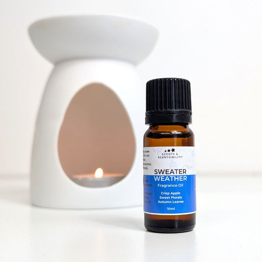 Bottle of 'Sweater Weather' fragrance oil with a lit wax warmer and oil burner on a white background