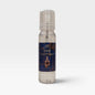 A clear plastic spray bottle of 'The Alchemist' body spray by Scents & Scentsibility, featuring a dark blue label with gold lettering and an illustration of an alchemy flask, set against a light gray background.