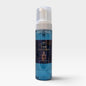 A bottle of The Alchemist Handmade Foaming Soap against a light gray background. The soap is a translucent blue liquid inside a clear bottle with a white pump dispenser and a dark navy label featuring gold text and illustrations.
