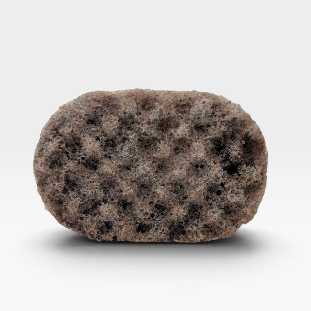 A textured, oval-shaped bath sponge with a mottled pattern of brown, beige, and black spongy material, shown on a clean white background with a soft drop shadow.