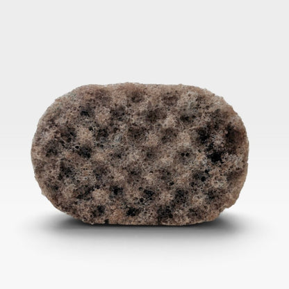 A textured, oval-shaped bath sponge with a mottled pattern of brown, beige, and black spongy material, shown on a clean white background with a soft drop shadow.