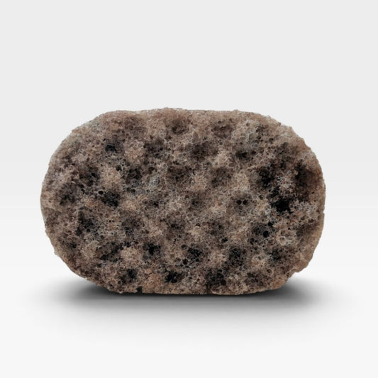 A textured, oval-shaped bath sponge with a mottled pattern of brown, beige, and black spongy material, shown on a clean white background with a soft drop shadow.