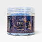 A clear plastic jar of Scents & Scentsibility 'The Alchemist' whipped soap, showing light blue soap layers and a dark blue label with gold text and celestial illustrations.
