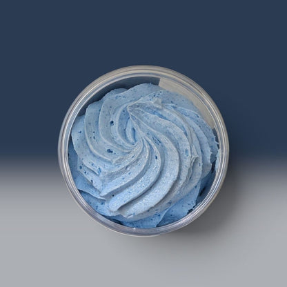 A top-down view of a light blue whipped soap product swirled inside a clear round plastic container, set against a dark blue gradient background.