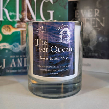 Candle labeled 'The Ever Queen: Roses & Sea Mist' with a blurred book in the background